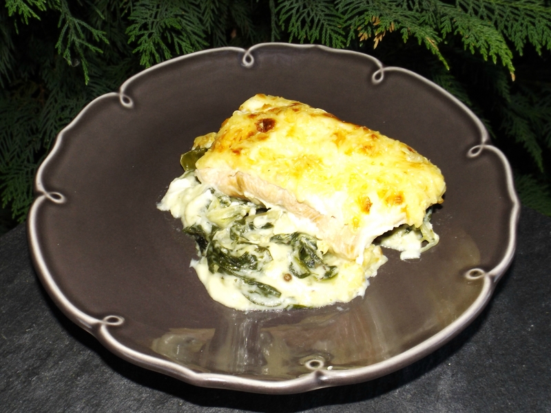 Gratin de saumon aux feuilles de blettes, servi sur une assiette sombre avec un fond crémeux aux blettes.