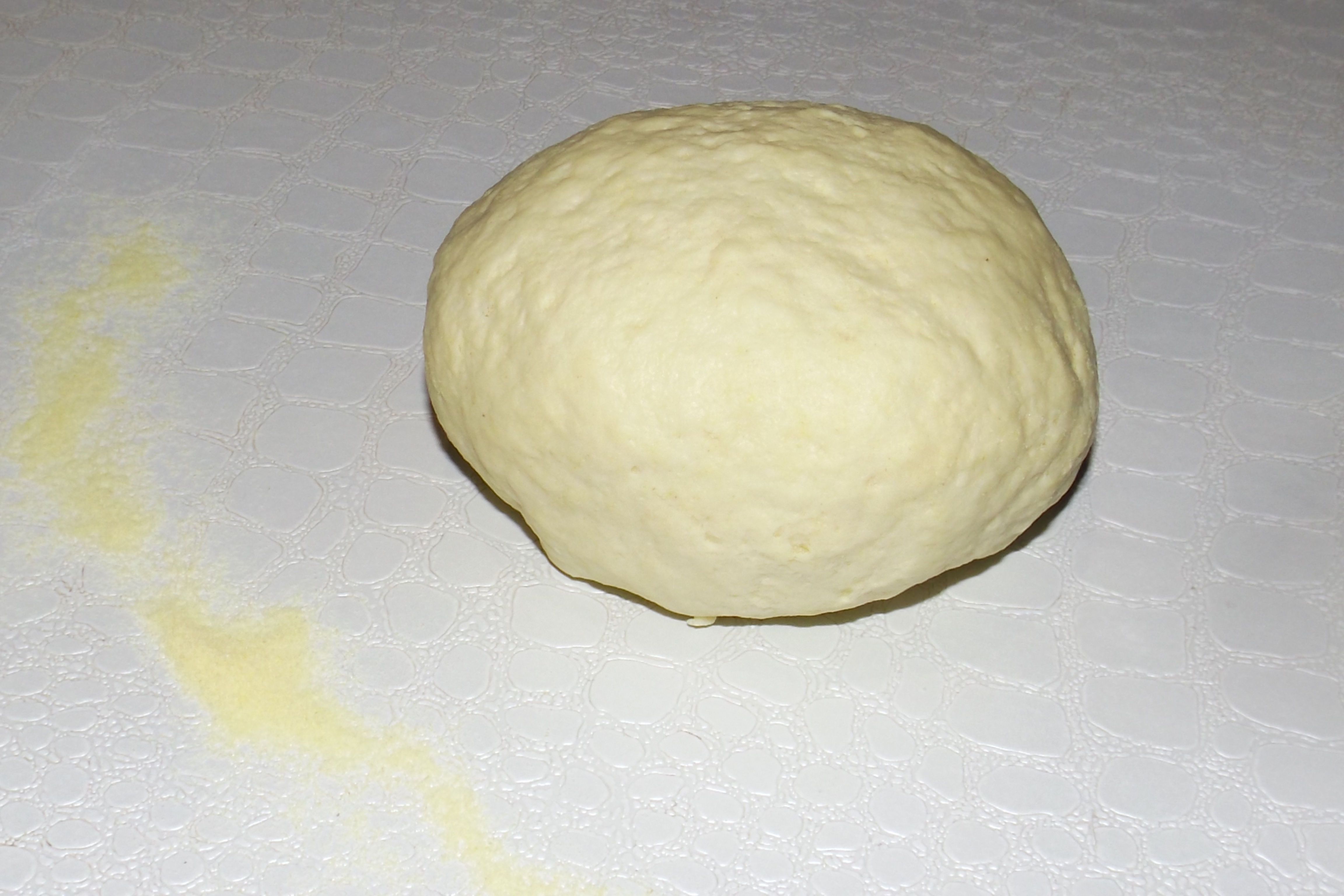 Photo d'une boule de pâte à pizza à la semoule, montrant sa texture lisse et légèrement jaune avant la cuisson.