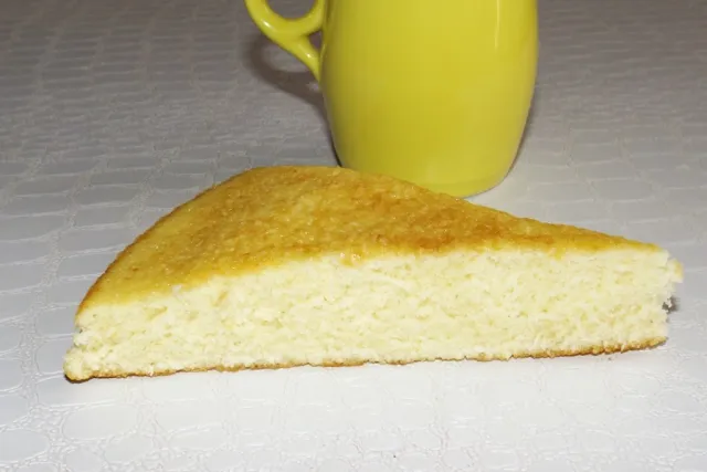 Une part de gâteau au lait chaud moelleux, coupée en triangle, avec une mie alvéolée et une croûte dorée, posée sur une table.