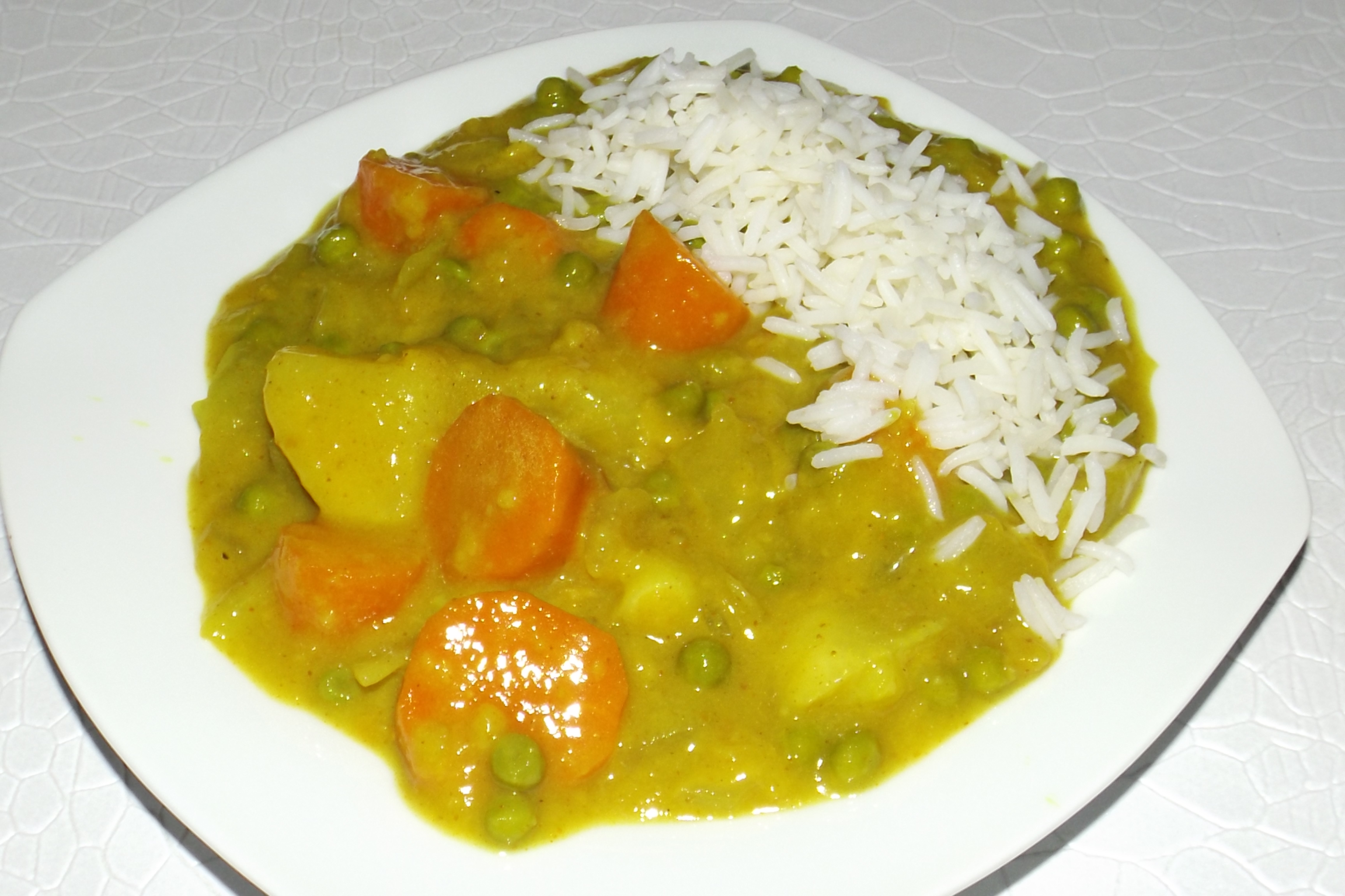 Assiette blanche contenant un curry de légumes japonais de Cyril Lignac, nappé de sauce, accompagné de riz blanc.